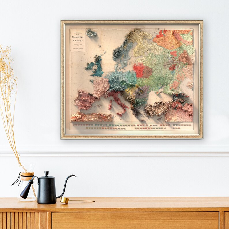 Op de afbeelding: Een vintage, ingelijste kaart van Europa met een 3D-effect. De kaart is gedrukt op cr&egrave;mekleurig papier en toont verschillende kleuren om verschillende regio's weer te geven. De titel van de kaart is "Carte Ethnographique de L'Europe".