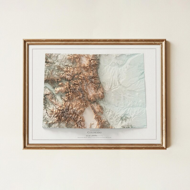K&ouml;nnte beinhalten: Gerahmte 3D-Topografische Karte von Colorado mit detaillierter Reliefdarstellung in Braun- und Wei&szlig;t&ouml;nen. Die Karte ist in einem goldfarbenen Rahmen und einem wei&szlig;en Passepartout eingefasst, geeignet f&uuml;r die Inneneinrichtung.