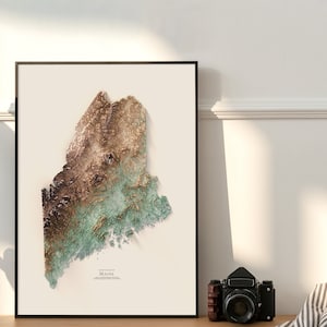 May include: A framed topographic map of the state of Maine. The map is in shades of brown, green, and gold, with a white background. The text "Elevation Map of Maine" is printed at the bottom of the map.