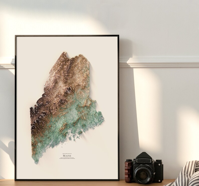 May include: A framed topographic map of the state of Maine. The map is in shades of brown, green, and gold, with a white background. The text "Elevation Map of Maine" is printed at the bottom of the map.