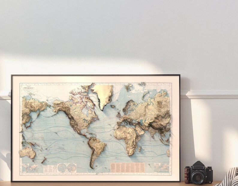 May include: A framed world map print featuring a three-dimensional relief effect. The landmasses are rendered in shades of gold and tan, contrasting against a light blue ocean background with thin, dark blue contour lines across the entire surface.