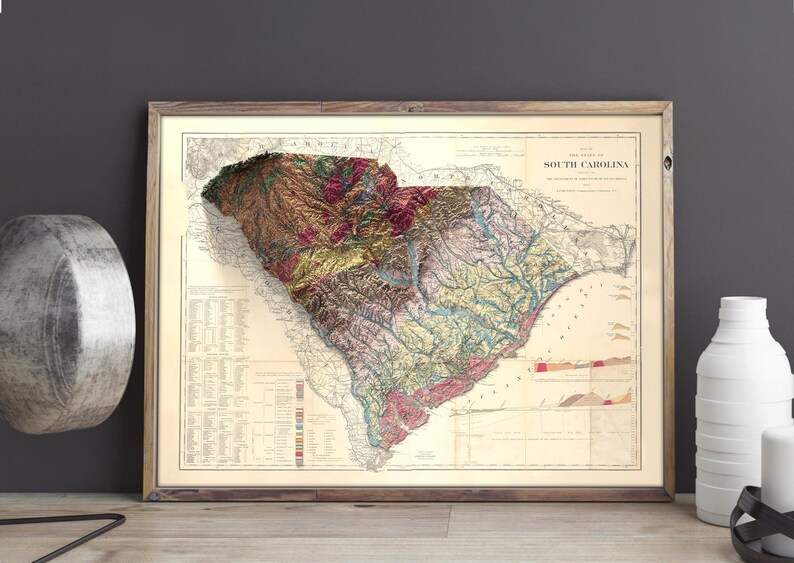 Pode incluir: Um mapa vintage da Carolina do Sul com um efeito de relevo 3D. O mapa &eacute; emoldurado em uma moldura de madeira marrom e tem um fundo creme. O mapa mostra a topografia do estado com diferentes cores representando diferentes eleva&ccedil;&otilde;es.