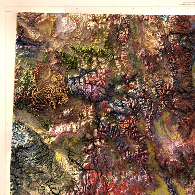 May include: A detailed, colorful topographic map of a mountainous region. The map features a variety of colors, including shades of green, brown, purple, and yellow, representing different elevations and geological features. The map is a detailed representation of the terrain.