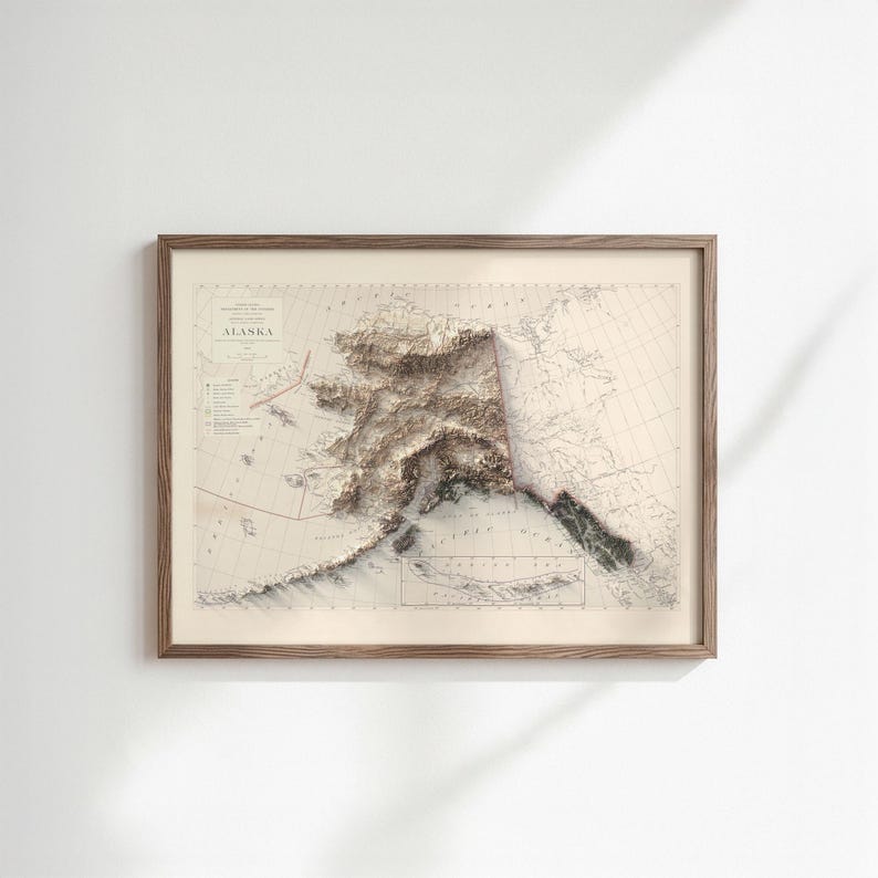 May include: Framed map of Alaska with a 3D topographic relief. The map is in a wooden frame and features detailed land elevation in shades of brown and beige. The word "Alaska" is printed at the top.
