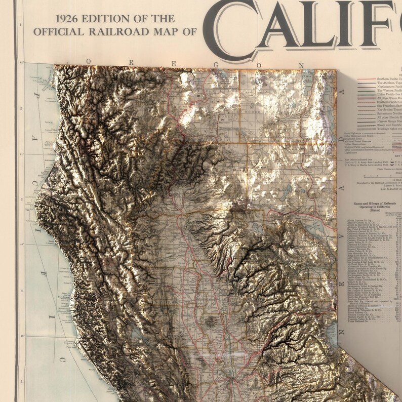 K&ouml;nnte beinhalten: Eine Vintage-Karte von Kalifornien aus dem Jahr 1926 mit dem Titel "1926 Edition of the Official Railroad Map of California". Die Karte zeigt die Topographie des Staates mit braunen und wei&szlig;en Schattierungen sowie ein Netz von Eisenbahnlinien in Rot und Schwarz.
