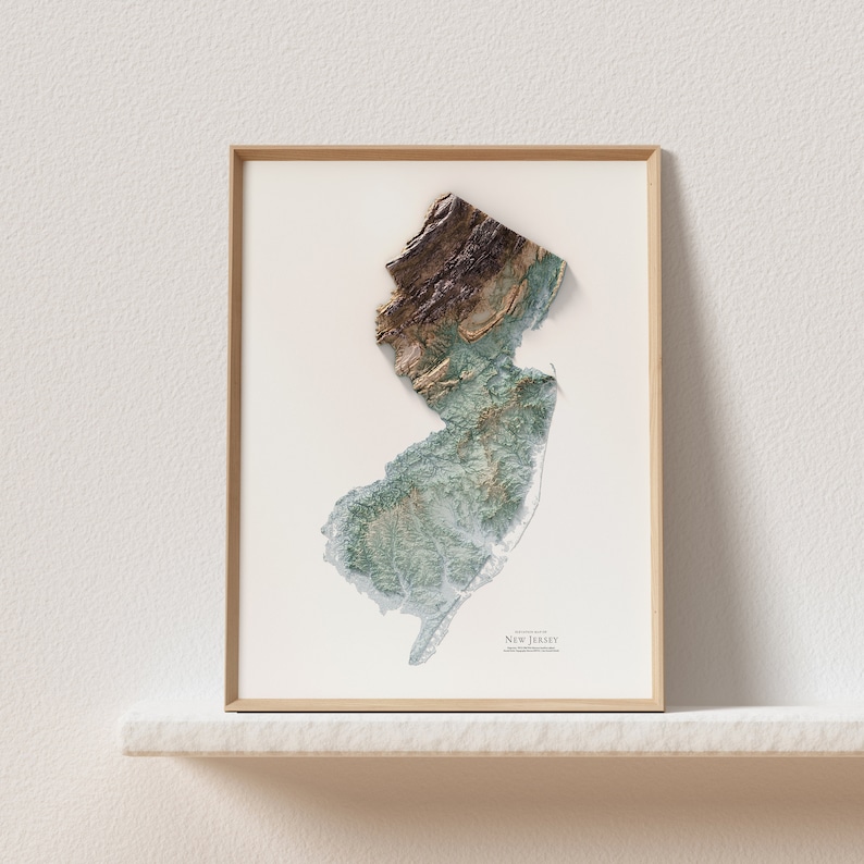 May include: A framed print of a topographic map of New Jersey. The map is in shades of green, brown, and white, and shows the state's terrain. The print is framed in a light wood frame.