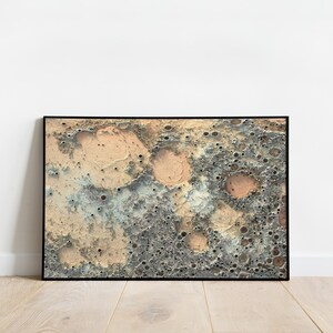 May include: A framed abstract print of a textured surface with craters and a color scheme of beige, gray, and blue.