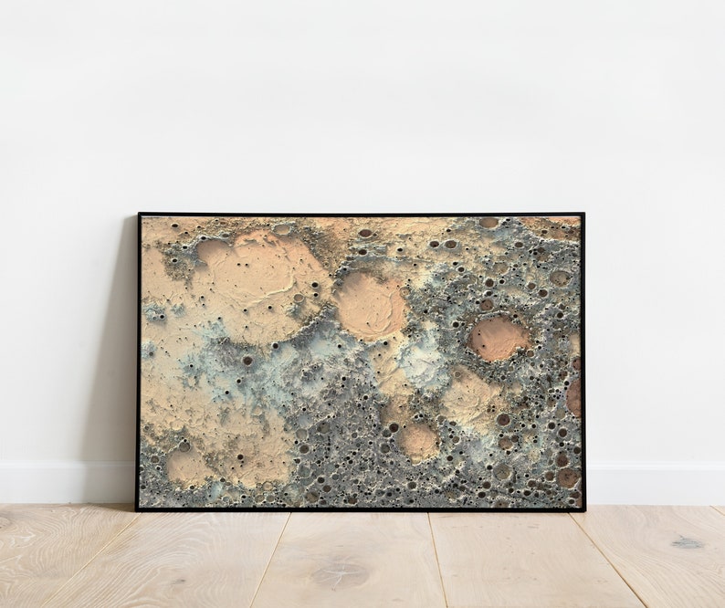May include: A framed abstract print of a textured surface with craters and a color scheme of beige, gray, and blue.