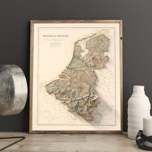 Pode incluir: Um mapa vintage da Holanda e da B&eacute;lgica em uma moldura de madeira. O mapa &eacute; em estilo relevo, mostrando a topografia da regi&atilde;o. O mapa &eacute; impresso em papel creme com acentos marrons e verdes.