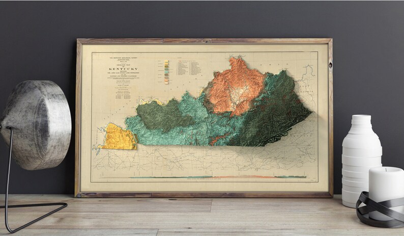 May include: A vintage map of Kentucky with a 3D relief effect, showing the state's topography with different colors representing elevation. The map is framed and hanging on a wall.