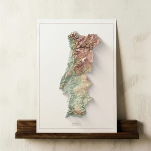 May include: A framed 3D relief map of Portugal, showcasing the country's topography in shades of green, brown, and pink. The map is mounted on a white background and displayed on a dark wooden shelf. The word "PORTUGAL" is printed at the bottom.