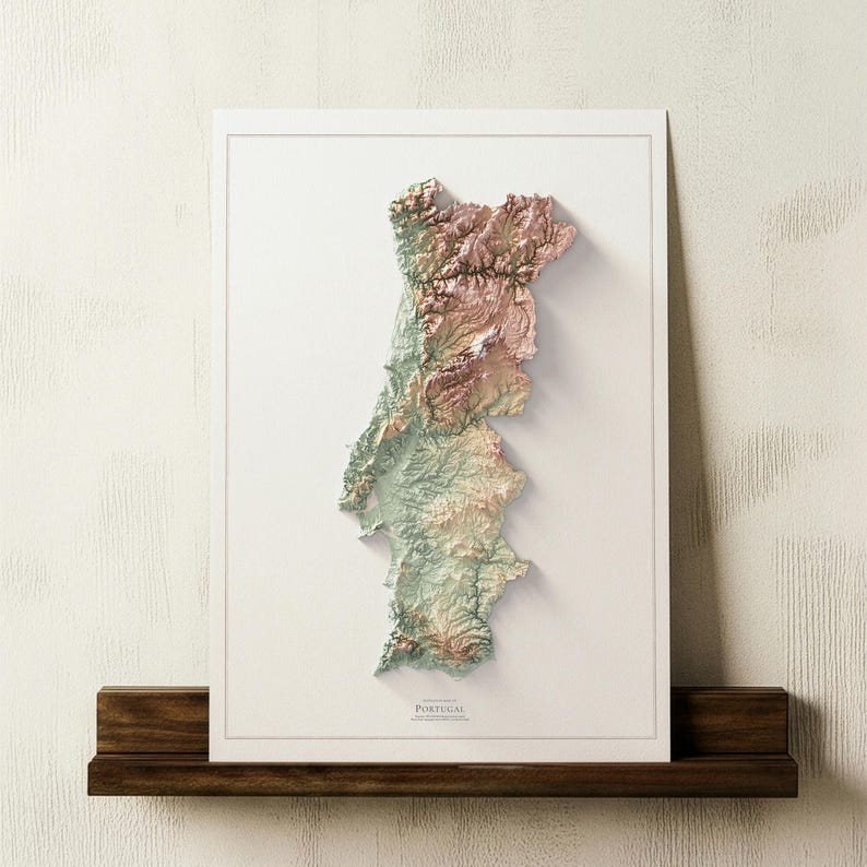 May include: A framed 3D relief map of Portugal, showcasing the country's topography in shades of green, brown, and pink. The map is mounted on a white background and displayed on a dark wooden shelf. The word "PORTUGAL" is printed at the bottom.
