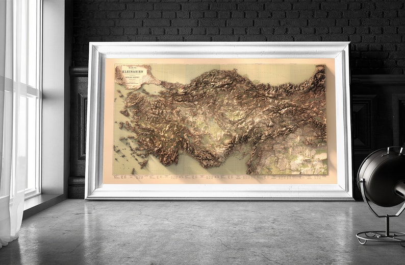 May include: A vintage, detailed relief map of Asia Minor, also known as Anatolia, with the title "Kleinasien" in German. The map is framed in a white frame and displayed against a black brick wall.