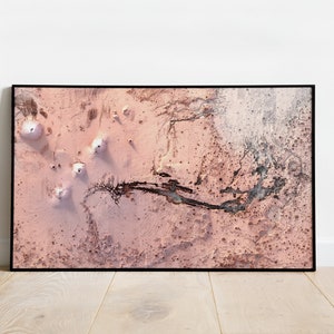 May include: An aerial photograph of a pink and white desert landscape with a winding riverbed. The landscape is dotted with small, white mounds.