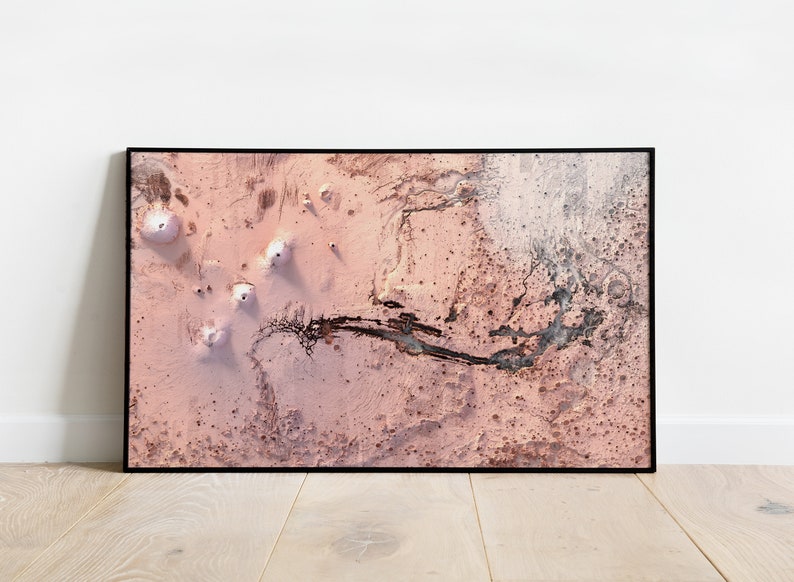 May include: An aerial photograph of a pink and white desert landscape with a winding riverbed. The landscape is dotted with small, white mounds.
