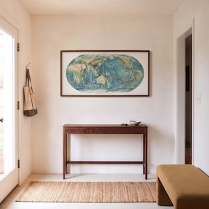 May include: A rectangular wooden console table with a single drawer, positioned beneath a framed oval world map print. The table features four slender legs and a horizontal support bar, crafted from dark brown wood with a smooth finish.