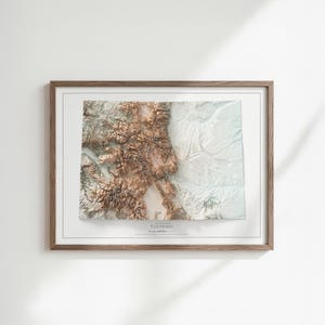 K&ouml;nnte beinhalten: Gerahmte topografische 3D-Karte von Colorado in Braun-, Wei&szlig;- und Blaut&ouml;nen. Die Karte ist in einem Holzrahmen eingefasst und tr&auml;gt den Namen des Staates. Das Kunstwerk ist auf einem wei&szlig;en Hintergrund montiert, geeignet f&uuml;r die Inneneinrichtung.