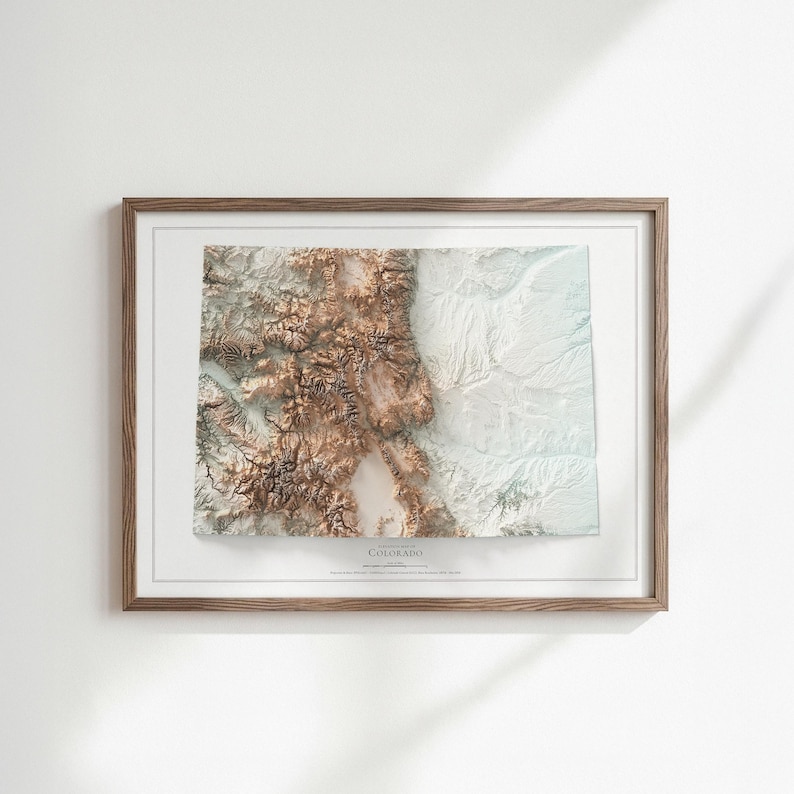 K&ouml;nnte beinhalten: Gerahmte topografische 3D-Karte von Colorado in Braun-, Wei&szlig;- und Blaut&ouml;nen. Die Karte ist in einem Holzrahmen eingefasst und tr&auml;gt den Namen des Staates. Das Kunstwerk ist auf einem wei&szlig;en Hintergrund montiert, geeignet f&uuml;r die Inneneinrichtung.