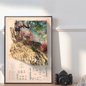 May include: A vintage-style topographic map of Arizona, framed in black. The map features a detailed relief depiction of the state's terrain, with various colors representing different elevations and geological formations. The map is titled "Topographic Map of Arizona" and includes a legend and scale.
