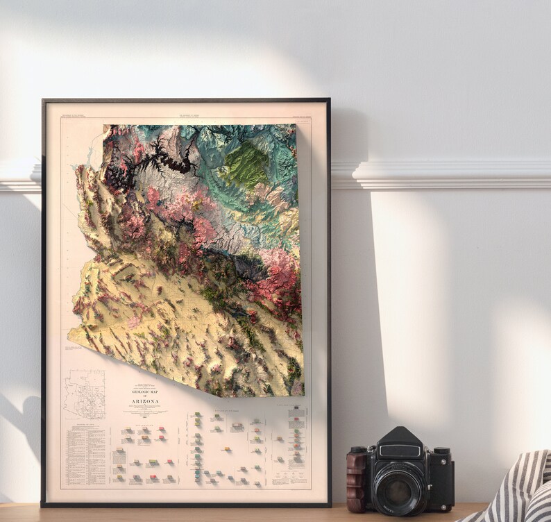 May include: A vintage-style topographic map of Arizona, framed in black. The map features a detailed relief depiction of the state's terrain, with various colors representing different elevations and geological formations. The map is titled "Topographic Map of Arizona" and includes a legend and scale.
