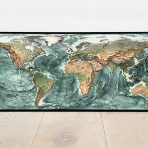 May include: A framed world map with a 3D effect, showing the continents in shades of green and brown, and the oceans in shades of blue.
