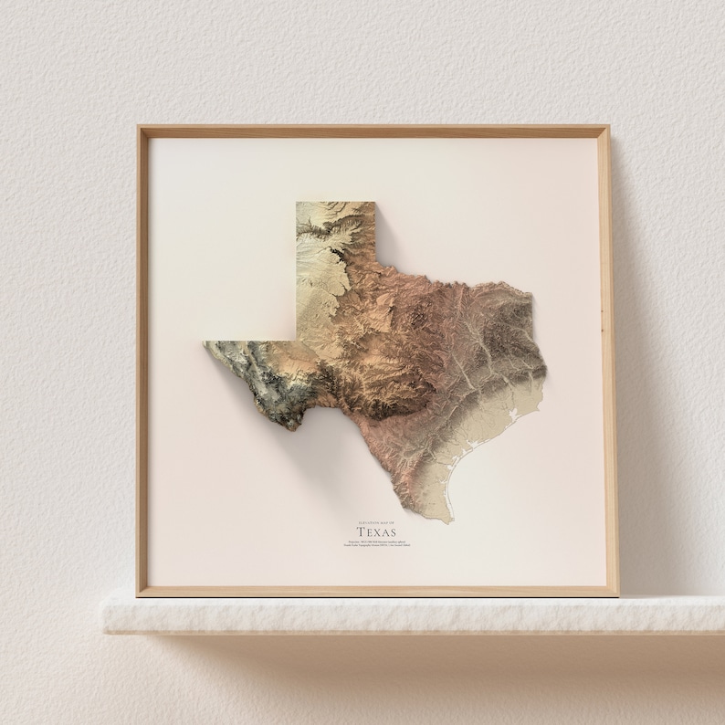 May include: A framed topographic map of Texas with a beige background and a brown wooden frame. The map is in shades of brown, beige, and green, showing the state's terrain.