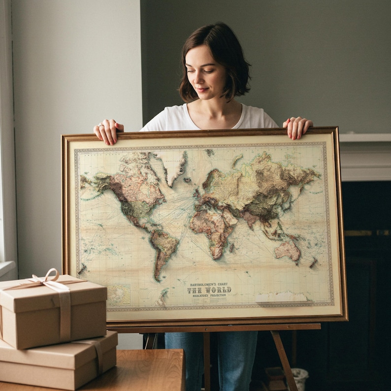 May include: A framed world map with a gold-colored frame. The map features a vintage style with detailed geographical features and is labeled "Bartholomew's Chart The World". The map is displayed on an easel.