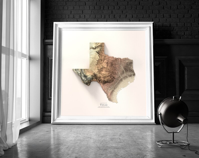 May include: A framed print of a topographic map of Texas. The map is in shades of brown, beige, and green, with a white background. The word "Texas" is printed in black at the bottom of the map.