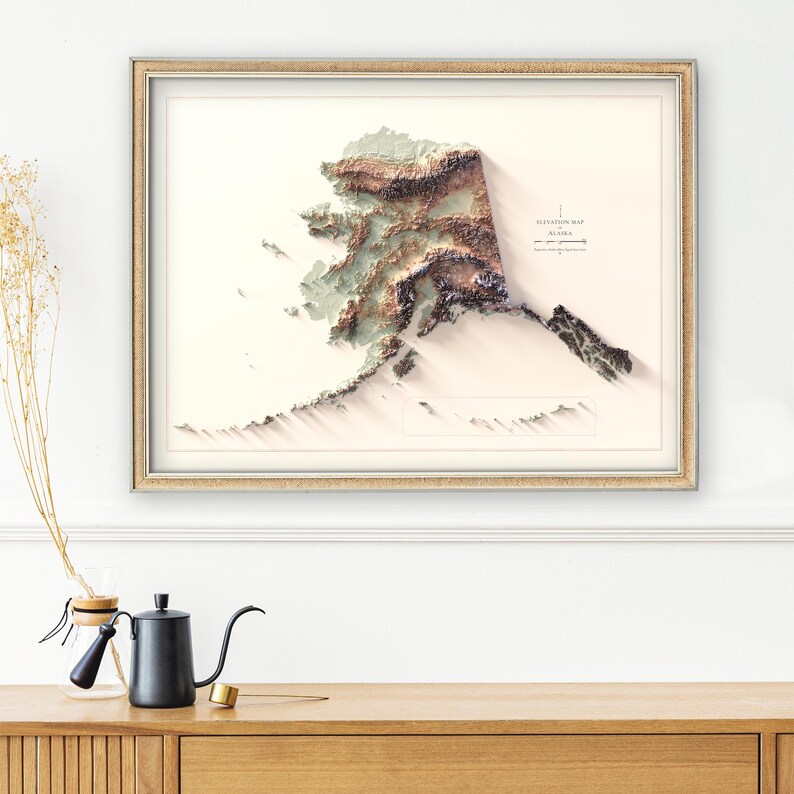 May include: Framed elevation map of Alaska, featuring a 3D relief design with shades of brown, green, and white. The map is set against a cream-colored background and enclosed in a gold-colored frame. The text "Elevation Map Alaska" is visible.