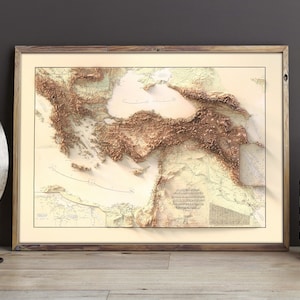 Pode incluir: Um mapa de relevo 3D emoldurado do Mar Mediterr&acirc;neo e das massas terrestres circundantes. O mapa &eacute; impresso em um fundo creme com detalhes topogr&aacute;ficos marrons e bege. A moldura &eacute; uma moldura de madeira simples com um acabamento marrom claro.