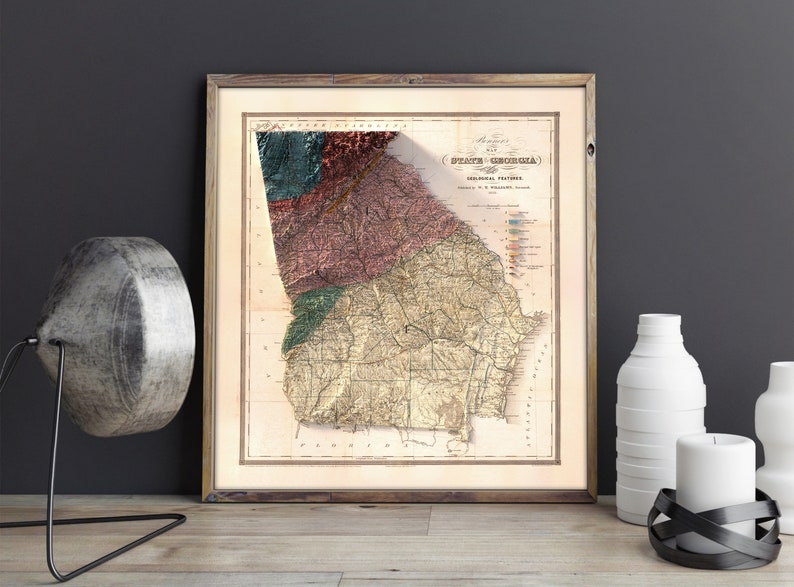 May include: An antique map of the State of Georgia, showing geological features. The map is printed in brown, green, red, and blue ink on a cream-colored paper. The map is framed in a wooden frame.