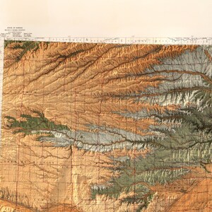 Puede incluir: Un mapa vintage del estado de Kansas, que muestra la topograf&iacute;a del terreno en marr&oacute;n, verde y blanco. El mapa est&aacute; dividido en cuadrados, con los nombres de los condados escritos en rojo.