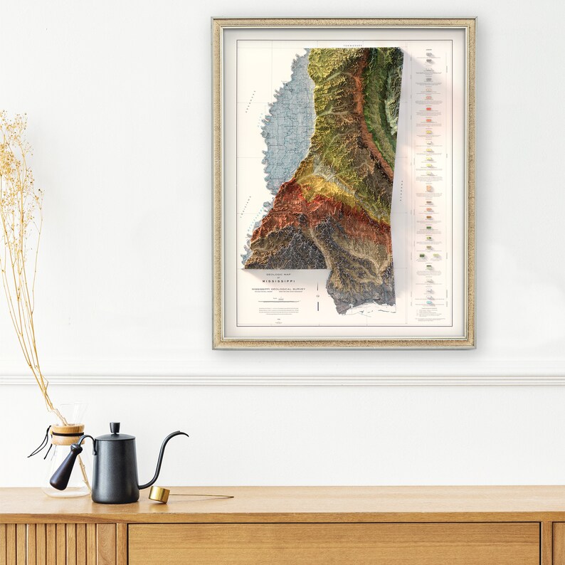 K&ouml;nnte beinhalten: Eine topografische Karte von Mississippi im Vintage-Stil in einem silbernen Rahmen. Die Karte ist auf wei&szlig;em Papier gedruckt und zeigt eine detaillierte Reliefkarte des Bundesstaates in Blaut&ouml;nen, Gr&uuml;n, Braun und Rot. Die Karte tr&auml;gt den Titel "Mississippi" und enth&auml;lt eine Legende und eine Skala.