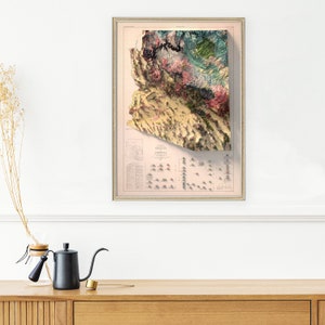 May include: A vintage, framed map of Arizona with a 3D relief effect. The map is printed in shades of brown, green, and pink, and shows the state's topography. The map is framed in a simple, gold-colored frame.