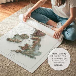May include: A detailed map art print of the British Isles, featuring a 3D topographic design in shades of brown and green. The map is on white paper, with the text "BRITISH ISLES" visible. The print is rolled up, with the text "HIGH - Quality 2D Map Art Prints" visible.