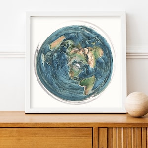 May include: A framed print of a detailed, three-dimensional rendering of Earth. The artwork features a blue and green color palette, showcasing continents and oceans. The print is displayed in a white frame, with a wooden sphere on the right.