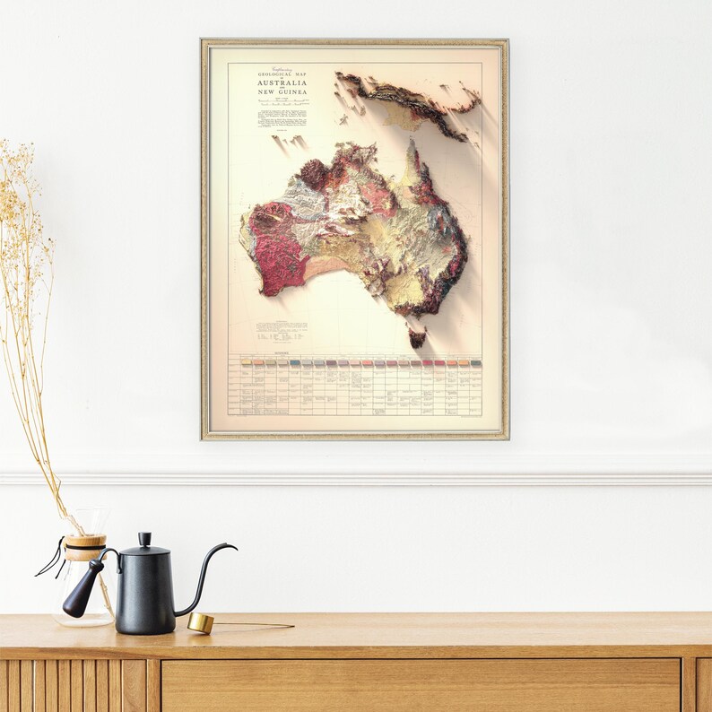 May include: A vintage map of Australia and New Guinea, showing the geological formations of the landmasses. The map is printed in shades of red, brown, and yellow, and is framed in a simple, cream-colored frame.