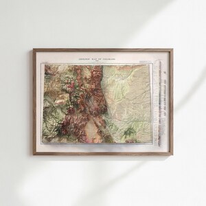May include: A framed vintage geological map of Colorado. The map features a detailed relief, showcasing the state's mountainous terrain in shades of brown, green, and beige. The map is encased in a wooden frame, adding a classic touch to the artwork.