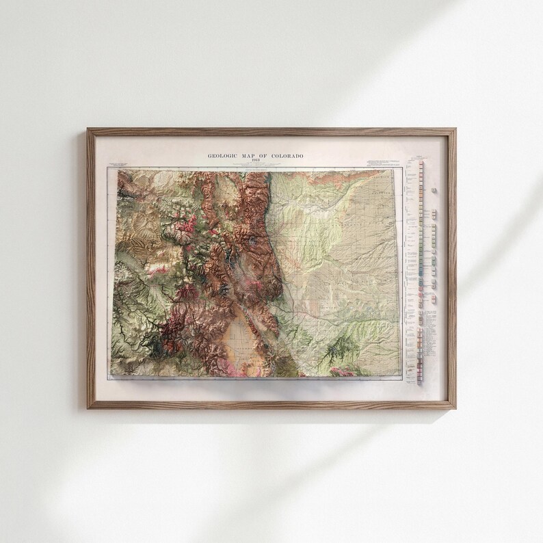 May include: A framed vintage geological map of Colorado. The map features a detailed relief, showcasing the state's mountainous terrain in shades of brown, green, and beige. The map is encased in a wooden frame, adding a classic touch to the artwork.