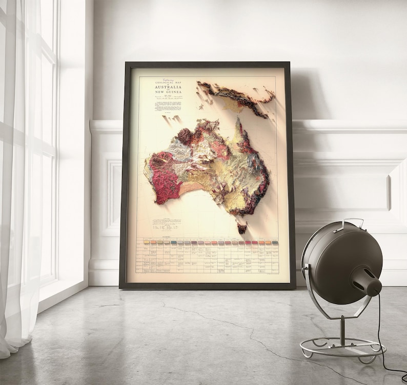 May include: A vintage-style relief map of Australia and New Guinea, printed on paper and framed in black. The map shows the terrain in shades of brown, red, and yellow.