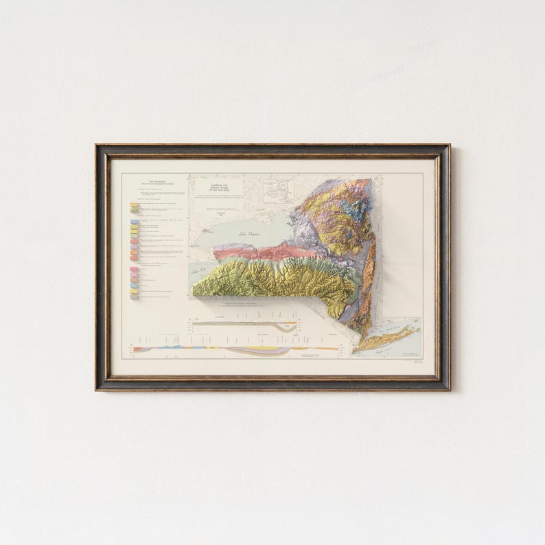Op de afbeelding: Ingelijste vintage kaart van de staat New York, met een gedetailleerd topografisch reli&euml;f. De kaart toont het gevarieerde terrein van de staat met kleuren die de hoogte weergeven. De kaart is ingelijst in een donkerhouten frame, klaar om te worden getoond.