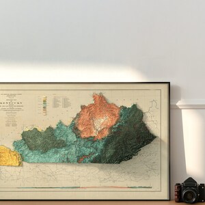 May include: A vintage, detailed relief map of Kentucky, showing the state's topography with different colors representing elevation. The map is framed in black and has a white background.