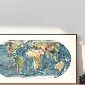 May include: A rectangular framed wall art print featuring an oval-shaped physical map of the world. The map displays continents in shades of green and brown, contrasted against deep blue ocean depths with visible topographical relief shading.