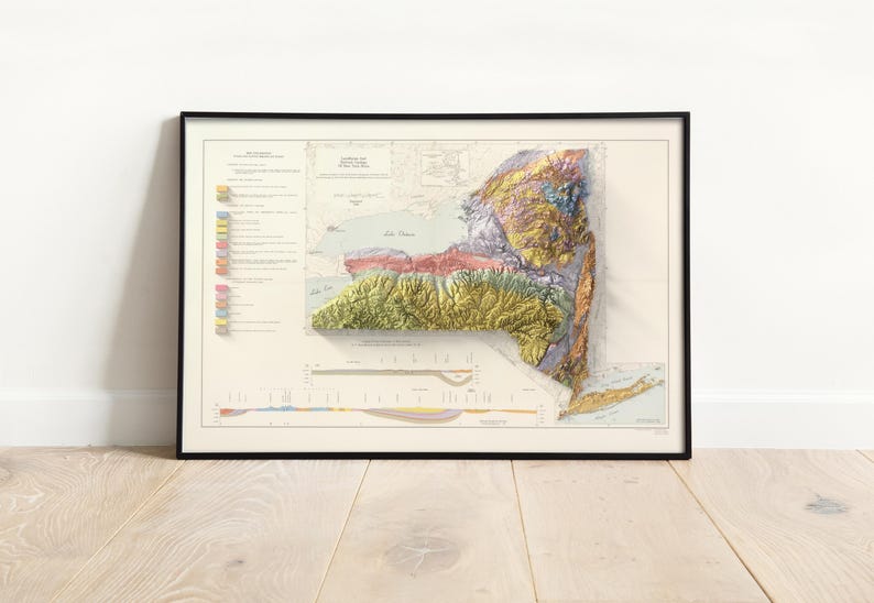 Op de afbeelding: Ingelijste 3D-reli&euml;fkaart van de staat New York, met topografische kenmerken in levendige kleuren. De kaart is ingelijst in een zwart frame en gemonteerd op een witte achtergrond. De kaart bevat gedetailleerde geografische informatie.