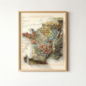 May include: Framed vintage geological map of France, featuring detailed relief and color-coded regions. The map is in a light wood frame, showcasing the topography of the French landscape. The title "Carte G&eacute;ologique de la R&eacute;gion Fran&ccedil;aise" is visible at the top.