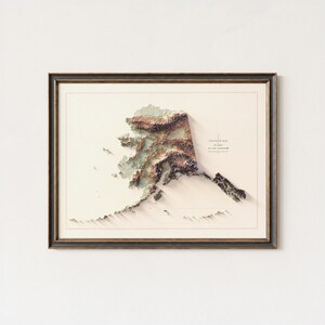 May include: Framed 3D elevation map of Alaska, featuring detailed topographical relief in shades of brown, green, and beige. The map is set against a cream background and enclosed in a dark brown frame, creating a striking visual representation.
