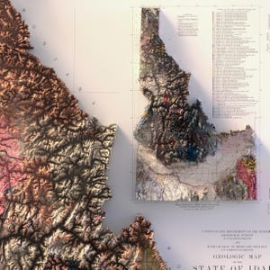May include: A detailed geologic map of Idaho, featuring a 3D topographic representation with varied colors. The map includes text indicating the United States Department of the Interior and the Idaho Bureau of Mines and Geology.