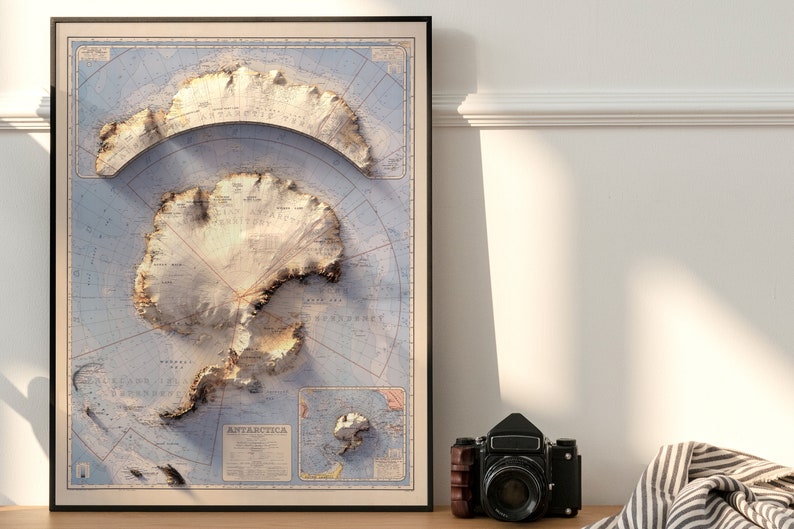May include: A vintage-style map of Antarctica with a 3D effect, showing the continent's topography and surrounding seas. The map is printed on a light blue background with brown and white details. The title "ANTARCTICA" is printed in the lower right corner.