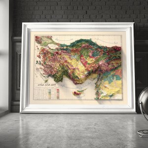 May include: A vintage map of Turkey with a relief-style design, showing the country's topography in shades of green, brown, and yellow. The map is framed in a white frame and is hanging on a wall.