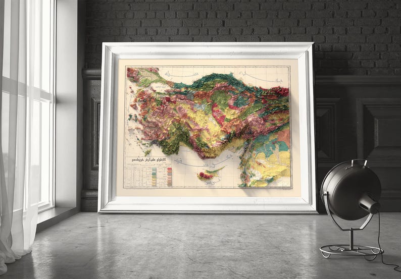 May include: A vintage map of Turkey with a relief-style design, showing the country's topography in shades of green, brown, and yellow. The map is framed in a white frame and is hanging on a wall.